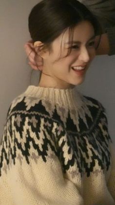 a woman smiling and wearing a sweater with an animal on it's back, in front of a white wall