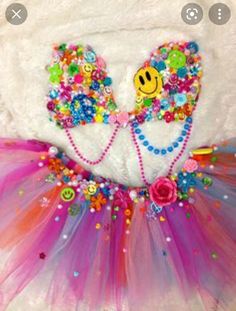 a white teddy bear wearing a colorful tutu with embellishments on it