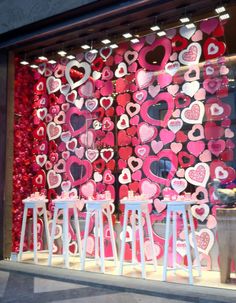 a store window decorated with hearts and stools for valentine's day display in front of it