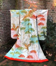 A spectacular example of a vintage Japanese formal wedding kimono, the outer-most garment thus referred to as a "robe," which a Japanese bride would wear over several other kimono layers, loosely draped and partly open at the bottom front (not tied with an obi belt). It is called an  known as "uchikake" in Japanese with its long "furisode" sleeves. Imagine this glorious garment hung on the wall decorating your home! The main design features Japanese red-crowned cranes (a symbol of filial piety and thus a symbol for marriage) swooping in and out of the pine tree boughs. All the cranes are painted and embroidered in gold while the pine branches alternate in red and green. The pine branch "shells" are filled with a traditional Japanese motif called "shippo" representing a tortoise shell. The Cream Silk Kimono For Wedding, Vintage Silk Kimono For Wedding, Cream Long Sleeve Kimono For Wedding, White Long Vintage Kimono, Long White Vintage Kimono, Bohemian Silk Kimono For Wedding, Bohemian Long Kimono For Weddings, Ceremonial Vintage Kimono, Vintage Long Kimono For Wedding