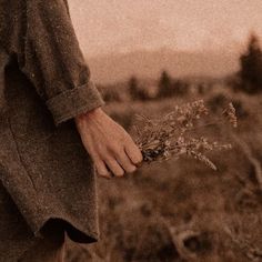 a person standing in a field with their hand on the ground and holding some plants