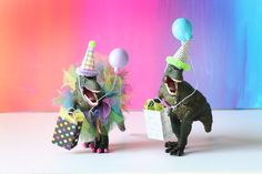 two toy dinosaurs wearing birthday hats and holding presents in their hands with balloons on them