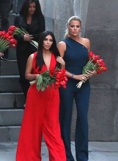 two women walking down the street with flowers in their hands and one woman wearing a blue jumpsuit