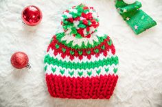 a red and green knitted hat sitting on top of a white blanket next to christmas decorations