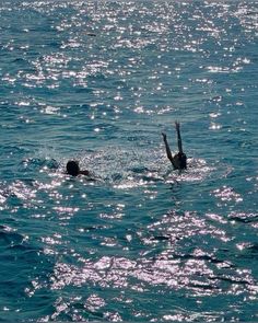 two people swimming in the ocean with their hands up and one person on his back