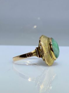 14K yellow gold ring with a natural jade. This vintage piece from the 70's is delicately made from the top of its scrolled shank to the textured bezel holding the stone in. The oblong oval Jade cabochon is a lovely green hue with white undertones. The basket is nice and opened eliminating any unnecessary weight. It measures 17mm x 12mm across the top and makes for the perfect statement ring. Finger size is 6.5 Feel free to message me if you have any other questions. Antique Oval Emerald Ring Stamped 14k, Oval Art Deco Emerald Ring Stamped 14k, Vintage Oval Emerald Ring For Formal Occasions, Formal Vintage Emerald Ring With Oval Cabochon, Vintage Oval Signet Ring With Bezel Setting, Antique Emerald Ring In Gold With Oval Cabochon, Art Deco Gold Oval Cabochon Ring, Gold Oval Emerald Ring In Art Deco Style, Antique Gold Emerald Ring With Oval Cabochon