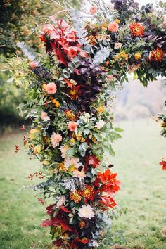 an arch made out of flowers and greenery in the middle of a grassy field