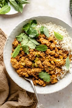 a white bowl filled with meat and rice topped with minty garnishments