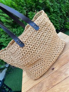 a straw bag sitting on top of a wooden table next to a green bush in the background