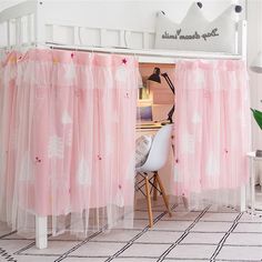 a room with a bed, desk and chair covered in pink tulle curtains that are hanging from the ceiling