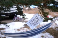 a sign hanging from a pine tree with snow on the ground and cars in the background