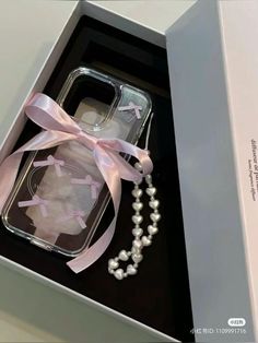 an open box containing a cell phone with a pink ribbon and pearls on the side