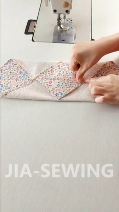 someone is sewing fabric on top of a table with a sewing machine in the background