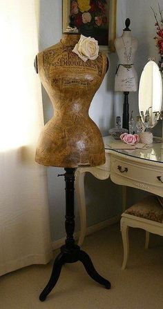 an antique mannequin is sitting on a stand in front of a mirror and desk