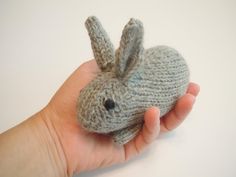 a hand holding a small gray knitted bunny