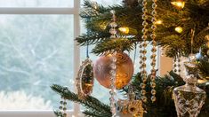 a christmas tree with ornaments hanging from it's branches in front of a window