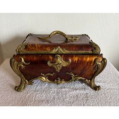 an ornate wooden box sitting on top of a white cloth covered table next to a wall