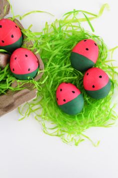 four watermelon painted rocks sitting in some green grass on top of a white surface