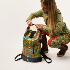 a woman kneeling down with a colorful backpack on her lap and the bag is open