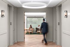 a man walking through an office lobby with two people sitting in chairs behind the glass door