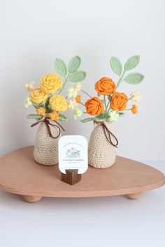 two crocheted vases with flowers in them on a wooden tray next to a card