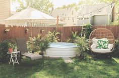 a backyard with a hot tub, chairs and umbrellas in the grass next to a fence