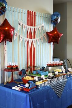 a blue table topped with lots of cake and dessert covered in red, white and blue balloons