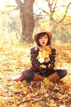 a woman sitting on the ground with leaves in front of her face and wearing a hat