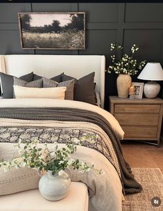 a white bed sitting in a bedroom next to a night stand with flowers on it