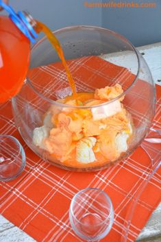 someone pouring orange juice into a bowl filled with food on top of an orange place mat