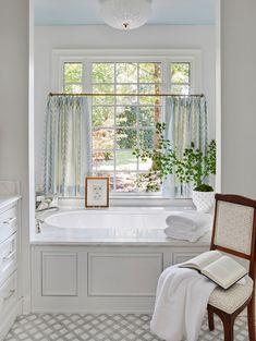 a bath room with a large window and a chair next to the tub in front of it