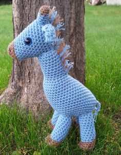 a crocheted toy horse standing next to a tree