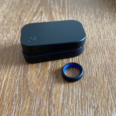 an open black box sitting on top of a wooden table next to a blue ring