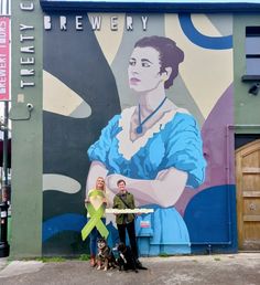 two people standing in front of a wall with a painting on it and a dog next to them