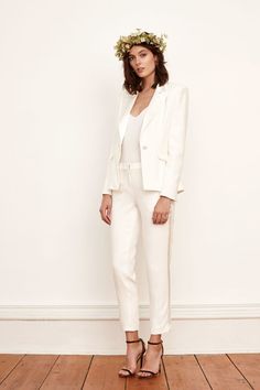 a woman standing in front of a wall wearing a white suit and floral headpiece