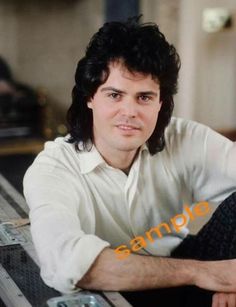 a man with long hair sitting on top of a table next to a cell phone