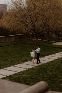 a man and woman standing on top of a lush green field next to a tree