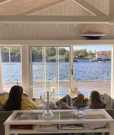 two women sitting on a couch looking out the window at water and boats in the distance