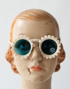 "Rare and iconic 1940s Daisy sunglasses. Off white with blue glass Crookes lenses. Thin elegant arms. Width: 4 7/8\"  Arm: 5\"  Note: Listing is for one pair. Pair you receive may not be the ones pictured, but differences are negligible.  Condition: Great! New Old Stock. Very wearable with some age related wear, as pictured.  - Temples slightly warped but does not effect wear. - Petals slightly warped, we find this to add to the whimsy and charm.  All sales are final, we can not predict how vint Daisy Sunglasses, Mannequin Head, Mannequin Heads, Blue Lenses, Sunglasses Vintage, Spectacles, Eyewear Sunglasses, Blue Glass, One Pic