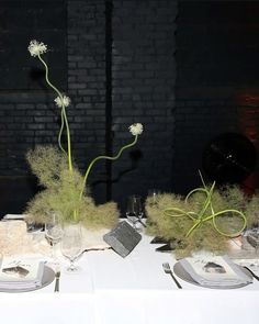 the table is set with white linens, silverware and tall grass plants in vases