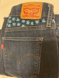 "These Levi's are uniquely embroidered with a medium blue and cream colored daisies. The style is \"shaping skinny\" with frayed bottoms. Although the jeans are not new they are in perfect condition.  Waist: 28 inches  Length: 26 inches  Style: shaping skinny with frayed bottoms  Wash: dark  Fly: Zip" Embroidered Dark Wash Mid-rise Bottoms, Embroidered Mid-rise Dark Wash Bottoms, Fitted Embroidered Dark Wash Jeans, Fitted Dark Wash Embroidered Jeans, Casual Fitted Bottoms With Embroidered Hem, Colored Daisies, Bill Blass Jeans, Hot Cold Packs, Cold Pack