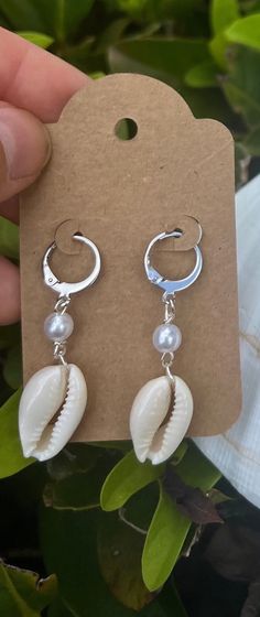 Handmade with real and authentic cowrie shells, these dangle earrings add an elegant and trendy look for any occasion. Choose gold or silver wiring and earring clasps.  Each seashell is meticulously handcrafted onto the earrings with a pearl colored bead and lever back clasps for a unique and organic element to your jewelry collection. Product Features: - Material: High-quality lever back clasp dangle earrings that are both durable and stylish, complemented by the authentic seashells for a disti Elegant White Cowrie Shell Jewelry, Handmade Silver Shell-shaped Pearl Earrings, Handmade Pearl Shell-shaped Earrings, Dangle Shell Earrings With Pearl Drop, Handmade Pearl Earrings In Shell Shape, Dangle Pearl Drop Shell Earrings, Pearl Drop Dangle Shell, Cowrie Shell Dangle Jewelry For Gifts, Cowrie Shell Dangle Jewelry Gift