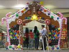 two people standing in front of a gingerbread house decorated with candy and candies