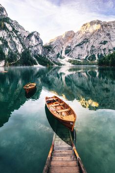 two small boats are docked at the end of a pier in front of some mountains