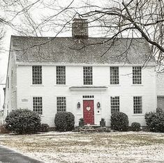 a white house with a red door and two windows in the front yard on a snowy day