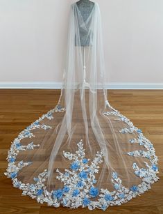 a wedding veil with blue flowers on it sitting on a wooden floor in front of a wall