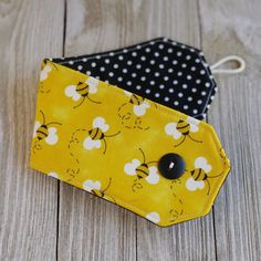 two small yellow and black bags on a wooden table with polka dotty fabric, one in the shape of a bee