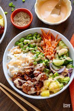 a bowl filled with rice, meat and vegetables next to chopsticks on a wooden table