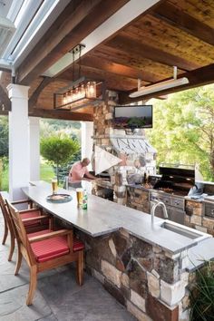 an outdoor kitchen and dining area with stone counter tops, red chairs, and wood ceilinging