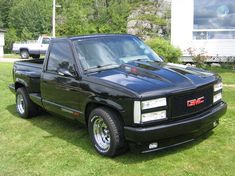 a black truck parked on top of a lush green field next to a white house